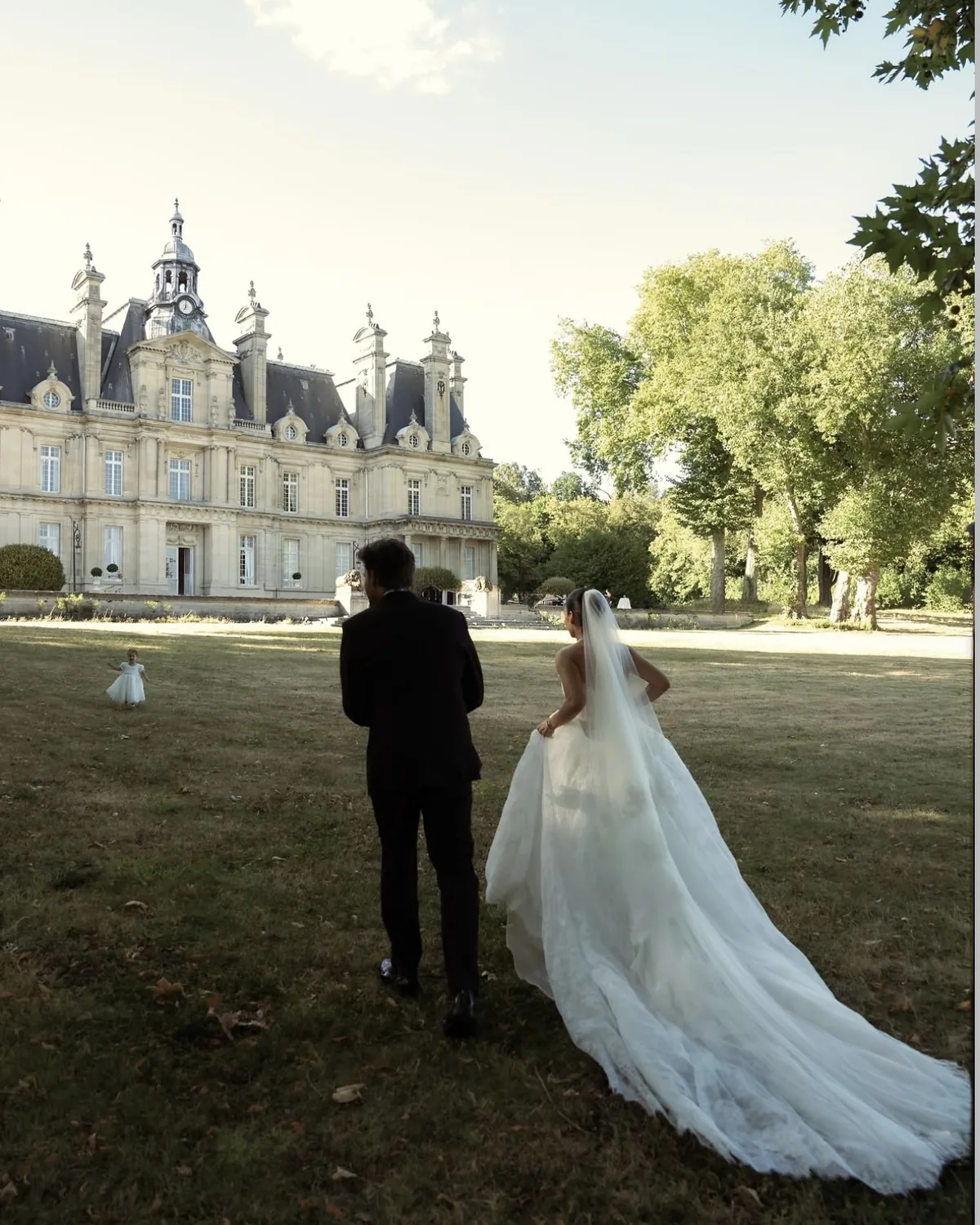 Danielle and Spencer walking the château lawn, her veil trailing behind her